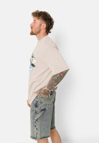 Lichtbeige T-shirt met korte mouwen en een grafische print, gecombineerd met grijze denim shorts met rafelige randen en meerdere zakken.