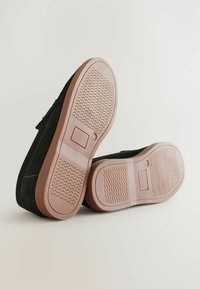Chaussures en suède noir avec une semelle en caoutchouc, présentant une semelle extérieure texturée marron. Le design comprend une silhouette simple et un profil bas.