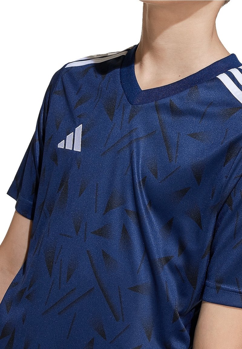 Mörkblå träningsskjorta med v-ringning, korta ärmar och geometriskt svart mönster. Har vitt varumärkeslogo på vänster bröst och axel.