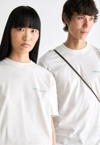 White cotton t-shirts feature a turquoise "tommy jeans" logo on the left chest. The design is casual with a classic crew neckline.