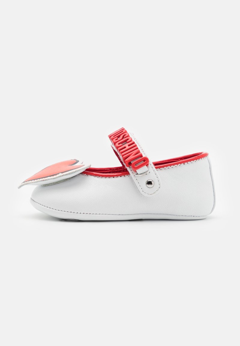 White leather shoe with red accents, rounded toe, side heart detail, and a strap featuring the brand name in raised letters.