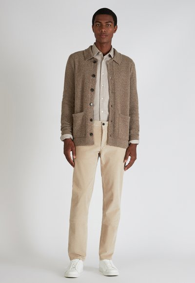 Beige textuur cardigan met een kraag, knoopsluitingen en twee voorzakken, gecombineerd met een licht shirt en crèmekleurige corduroy broek.