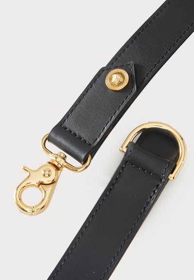 Čierny kožený remienok so zlatými kovaniami, vybavený karabínou a kruhovým krúžkom. Obsahuje dekoratívny zlatý emblém.