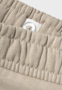 Cinturilla de tela beige con textura fruncida y un cierre de botón blanco con costuras a juego. Primer plano del material.