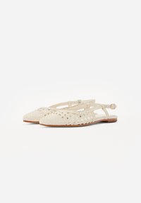 Chaussures plates blanches tissées avec un bout pointu, présentant un design de lanières entrecroisées et une petite boucle à la cheville. La semelle intérieure est de couleur claire.