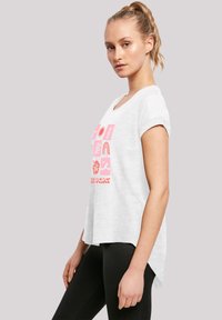 White short-sleeve T-shirt with a scoop neckline, featuring pink graphic designs and text, slightly curved hem, paired with black leggings.