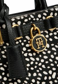 Zwart-wit gevlekte handtas gemaakt van textuurleer, met gouden hardware en een ronde logo-accent.