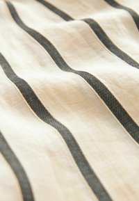 Tissu rayé en beige et gris foncé, présentant des lignes ondulées prononcées et une surface texturée. Le matériau semble doux et léger.