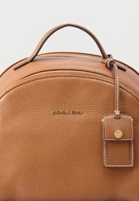 Tan textured leather handbag with a top handle, gold zipper, Michael Kors logo, and stitched leather tag with gold MK button.