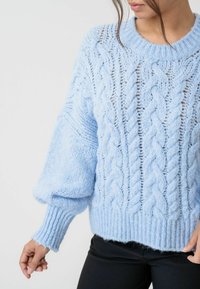 Ljusblå kabelstickad tröja med överdimensionerade ärmar, ribbade muddar och en avslappnad passform. Har ett strukturerat mönster och en öppen väv.