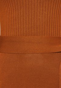 Ribbat, djupt orange tyg med en slät, kontrasterande midjeband. Texturen är mjuk och elastisk, perfekt för åtsittande kläder.