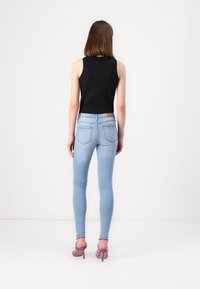 Top negro sin mangas, jeans ajustados de color azul claro y sandalias de tacón moradas. El conjunto presenta un diseño ajustado y detalles sutiles.