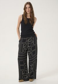 Black tank top paired with wide-leg pants featuring a bold white geometric pattern. Material appears soft with a relaxed fit. Flats complete the outfit.