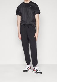 Černé pruhované tričko s krátkými rukávy a malým logem, spárované s černými tepláky a černočervenými teniskami. Neformální sportovní outfit.