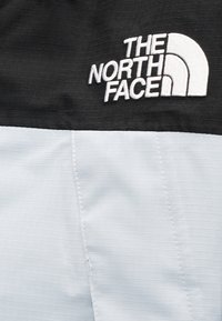 Φωτεινό μπλε και μαύρο μπ ουφάν με κάθετη ριμπ υφή· διαθέτει κεντημένο λογότυπο «The North Face» σε μαύρο ύφασμα στον ώμο.