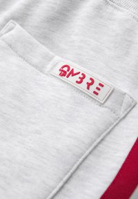 Sudadera gris clara con un bolsillo, tejido texturizado, acento rojo horizontal y una etiqueta roja y blanca con "LEVEL UP" y "ON3RE."