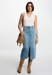 Top de tirantes acanalado en gris claro con escote en forma de ondas, combinado con una falda maxi de denim azul con una abertura frontal. Botas de ante marrón hasta la rodilla y un bolso de flecos.