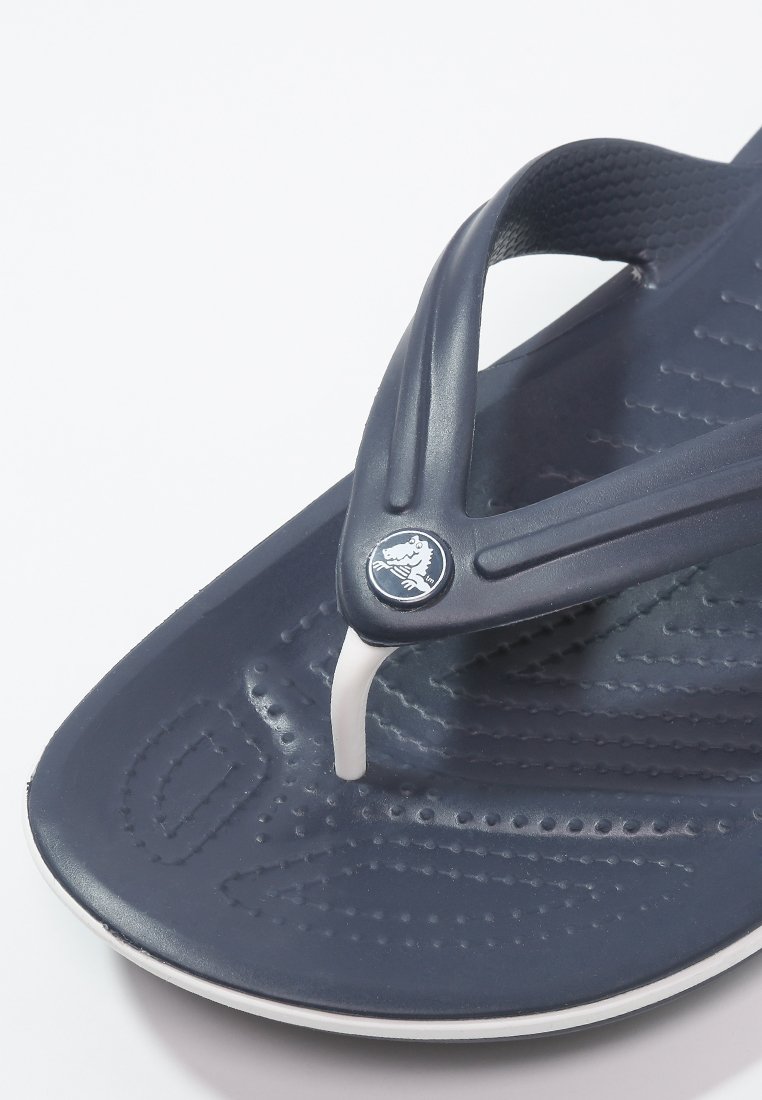 Chanclas navy con una suela texturizada y tira blanca. Presenta un logotipo circular en la tira. El material parece goma y flexible.