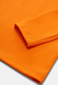 Orange langærmet skjorte med en glat tekstur, der har en fold ved manchetterne og flade sømme. Enkelt design uden mønstre eller accenter.