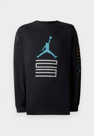 Musta pitkähiha t-paita, joka on valmistettu puuvillasta. Paidassa on sininen Air Jordan -logo ja graafinen kuvio, ja hihoissa on valkoista ja kultaa tekstiä.