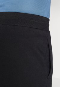 Čierne joggingové nohavice s rebrovaným pásom, obsahujúce bočnú vrecko. Tkanina vyzerá hladko s jednotnou textúrou.