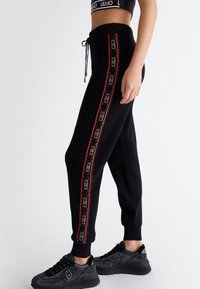 Schwarze Jogginghosen mit rot gestreiften Seitenbesätzen, ausgestattet mit einem Muster, einem elastischen Bund mit Kordelzug und ribbed Bündchen.