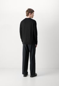 Black knitted sweater with ribbed hem and sleeves, paired with loose-fitting dark trousers. Smooth texture, relaxed silhouette.