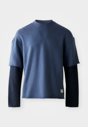 Mørkeblå sweatshirt med korte Ærmer, der har en kontrasterende lang mørkeblå ærme under. Lavet af blødt stof, minimalistisk design.