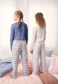 To piger iført hjemmebeklædning: den ene i en blå top med vaffeltekstur og ternede bukser, den anden i en hvid top og stribede bukser.
