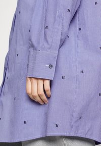 Lilla stribet skjorte med broderede accenter. Har en knappet manchet og en afslappet pasform, der fremhæver fine linjer og en glat tekstur.