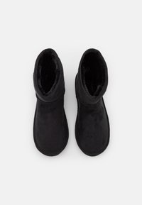 Pár černých zimních bot na slip-on s měkkou, fleecovou podšívkou, viděný z vrchu na jednobarevném bílém pozadí.