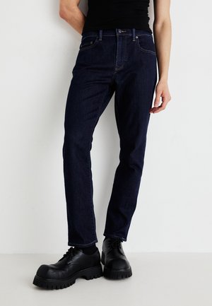 Jeanși din denim albastru închis, cu croi slim, având un design clasic cu cinci buzunare, cusături discrete și închidere cu buton. Asortați cu încălțăminte masivă neagră.