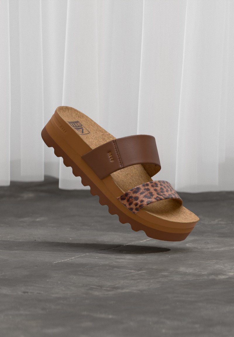 Καφέ πλατφόρμα σανδάλι με δύο λουριά, ένα μονόχρωμο καφέ και ένα με λεοπάρ σχέδιο, φελλό σε σόλα και οδοντωτή σόλα σε γκρι φόντο.
