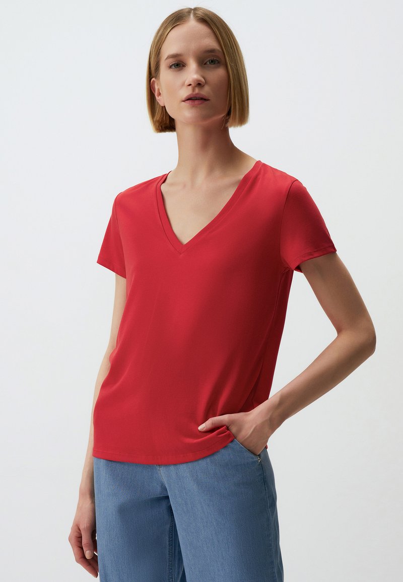Rode V-hals T-shirt van soepel materiaal met korte mouwen, gecombineerd met lichtblauwe denim. Heeft een relaxed fit en een eenvoudig ontwerp.