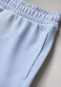 Lyseblå joggingbukser med elastisk taljebånd og sidelomme på en neutral baggrund.