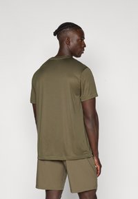 Olíva zöld, rövid ujjú ing könnyű anyagból, kerek nyakkal és laza fazonnal. Az ing azonos olíva zöld rövidnadrággal van párosítva.