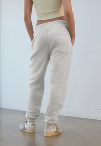 Ljusgrå mjukisbyxor med ledig passform, elastisk midjeband och mudd vid anklarna. Kombinerade med beiga sneakers med blå detaljer.