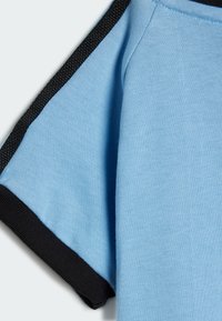 T-shirt di cotone azzurro chiaro con maniche corte e bordo in rib con trama nera lungo le cuciture. Struttura liscia, vestibilità casual e scollatura arrotondata.