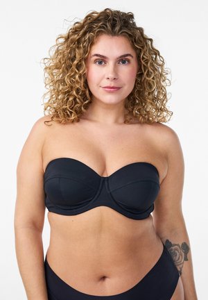 Woman with curly blonde hair wearing a black strapless bra and matching underwear, showing a rose tattoo on her left forearm.