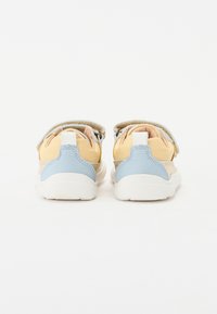 Baskets légères avec un dessus en textile jaune et beige, des accents en cuir bleu et des semelles blanches. Présente des straps à double attache auto-agrippante.