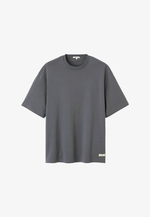 T-shirt gris foncé à manches courtes avec col rond et une petite étiquette rectangulaire près de l'ourlet inférieur sur le côté droit devant.