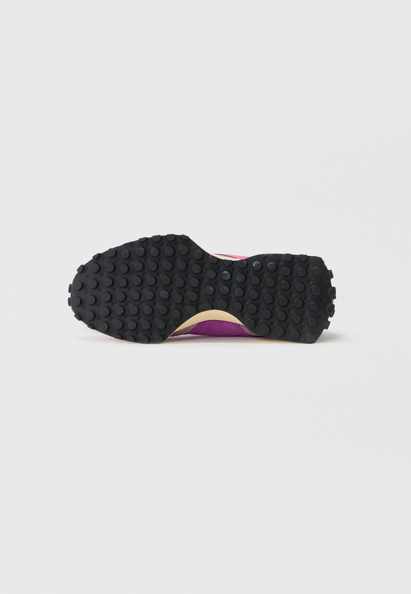 Semelle de chaussure de sport avec une surface en caoutchouc noir texturé et de petites grips circulaires. Accents violet vif visibles sur les bords.