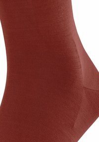 Calza marrone a costine, caratterizzata da una texture liscia e di altezza media. Il tessuto è elastico, garantendo una vestibilità aderente attorno alla caviglia.