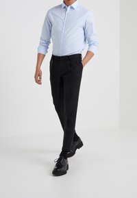 Světle modrá košile s dlouhým rukávem, černé kalhoty na míru s bočními kapsami a černé šněrovací boty, což vytváří smart-casual outfit.