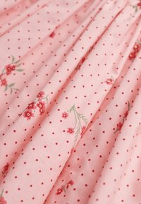 Lyserødt stof med hvide polkaprikker og små røde blomsterprint. Blød tekstur med folder, der skaber et draperet udseende.