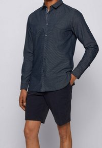 Mörkblå långärmad skjorta med knappar i en texturerad tyg, en bröstficka och mörka knappar. Kombination med marinblå shorts.