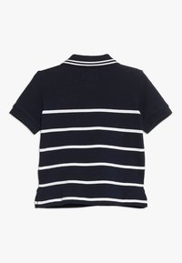 Námořnické polo tričko s bílými vodorovnými pruhy, vybavené klasickým límečkem a krátkými rukávy. Vyrobeno z texturované bavlněné tkaniny.