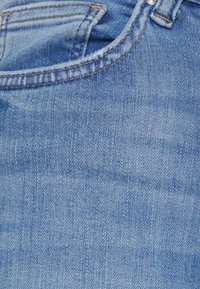 Jeans de ganga azul claro com uma textura suave, desvanecimento subtil e costuras visíveis ao longo da cintura e dos bolsos.