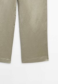 Pantalons beiges à jambes droites avec des coutures visibles le long des côtés intérieurs et extérieurs, présentés sur un fond blanc.