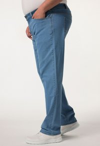 Jeans de mezclilla azul claro con corte recto, cinco bolsillos y un ligero desgastado. Llevados con zapatillas deportivas blancas, vistos de lado.